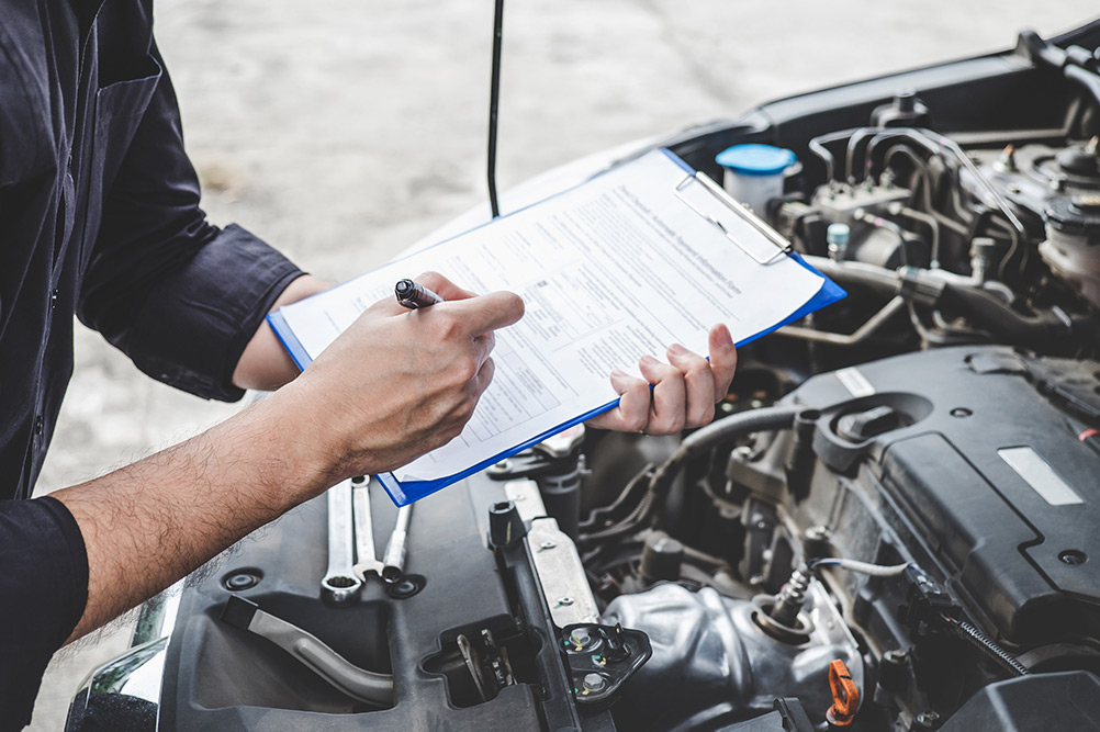 Close up of mechanic doing car diagnostics on clipboard above open car hood